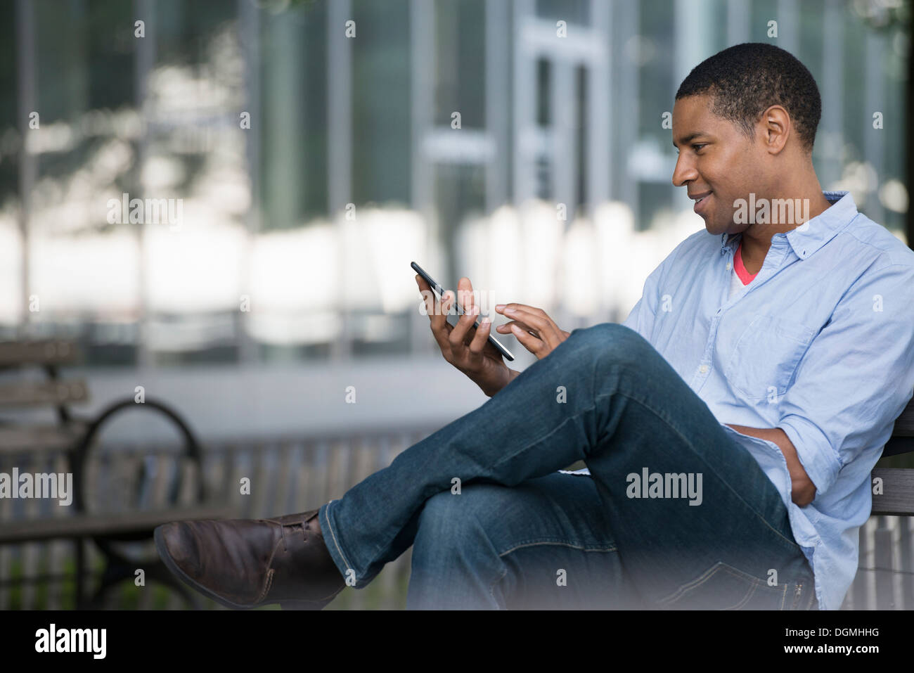 Sommer in der Stadt. Menschen im Freien, reibungslose Kommunikation unterwegs. Ein Mann sitzt auf einer Bank mit einem digitalen Tablet. Stockfoto