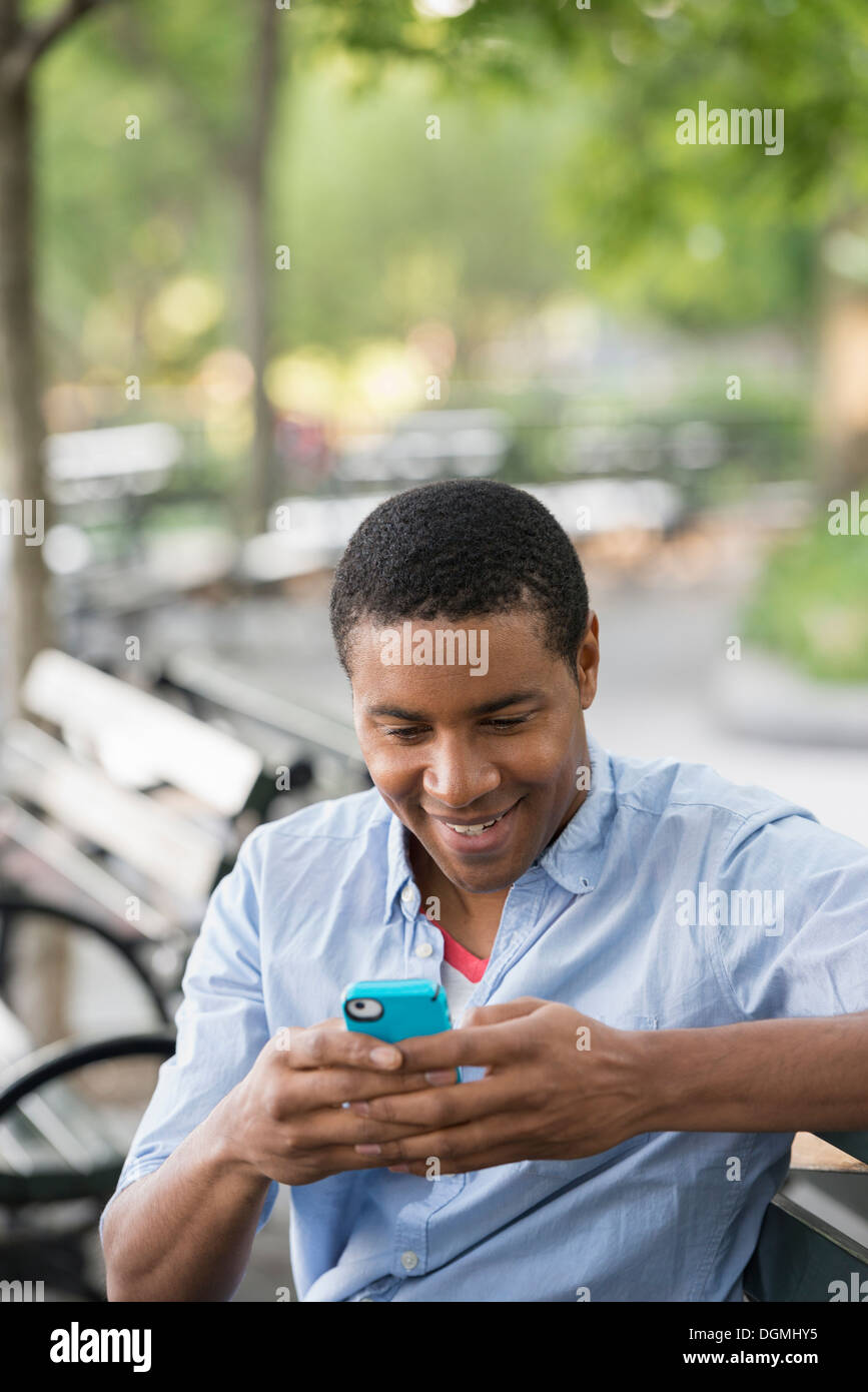 Sommer in der Stadt. Ein Mann sitzt auf einer Bank mit einem Smartphone. Stockfoto