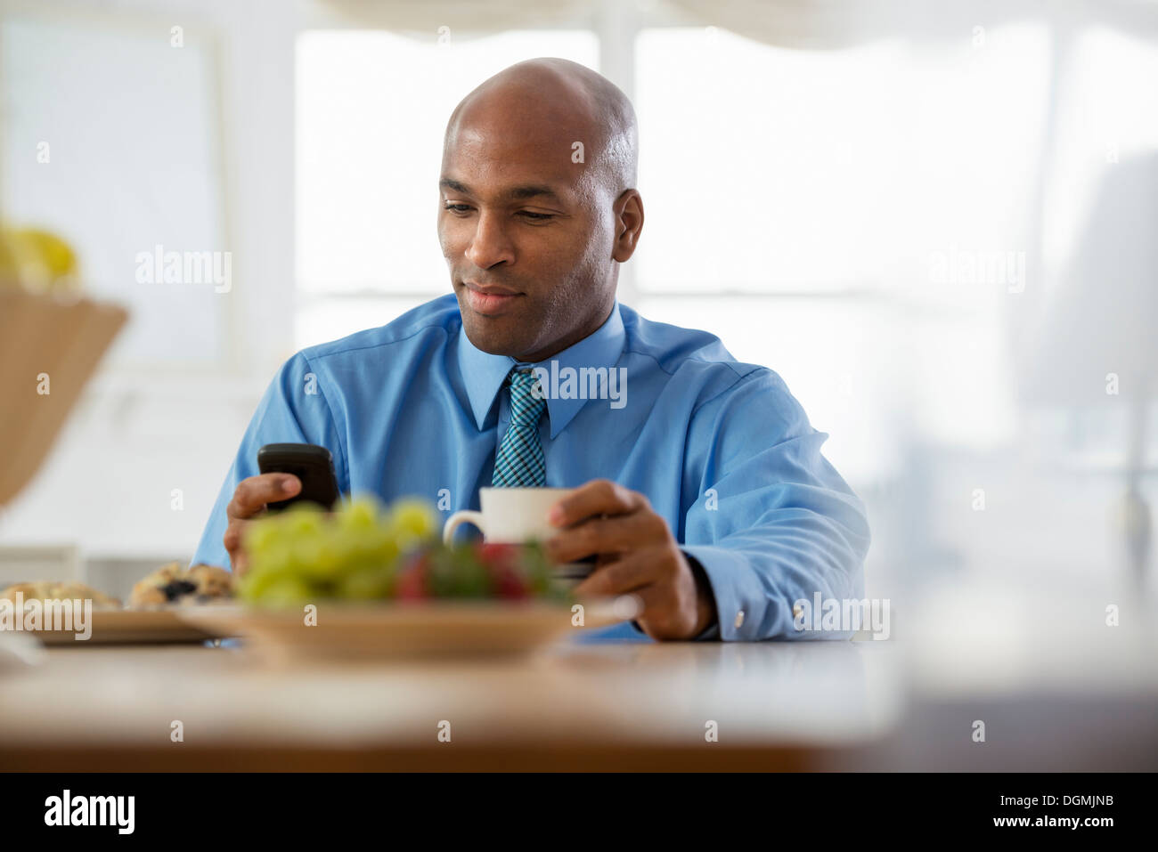 Ein Mann in einem blauen Shirt, sitzen an einem Frühstück bar mit einem Smartphone. Stockfoto