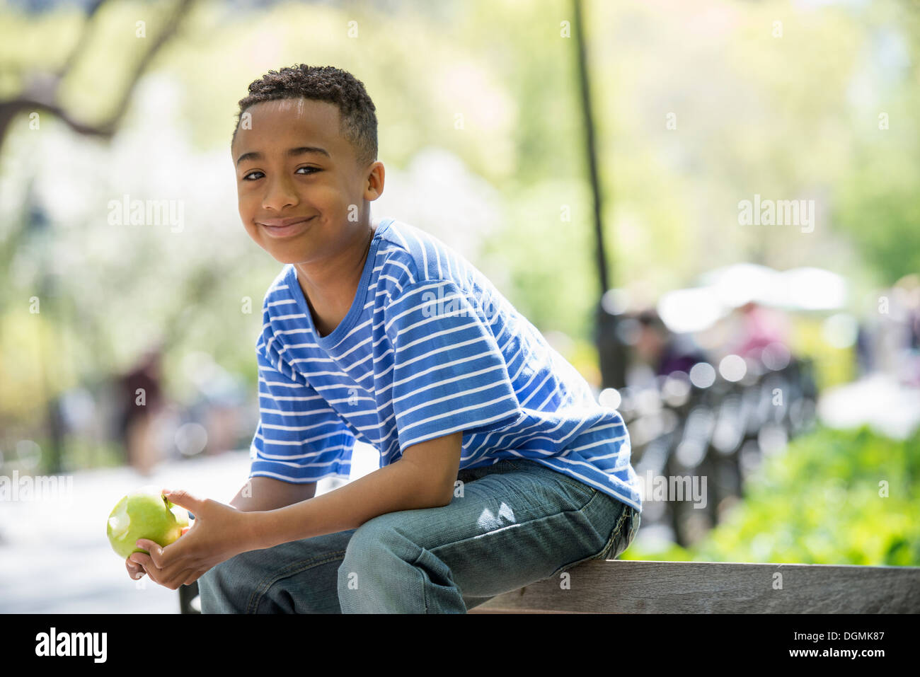 Eine Familie im Park an einem sonnigen Tag. Ein Junge sitzt auf einem Zaun einen Apfel essen. Stockfoto
