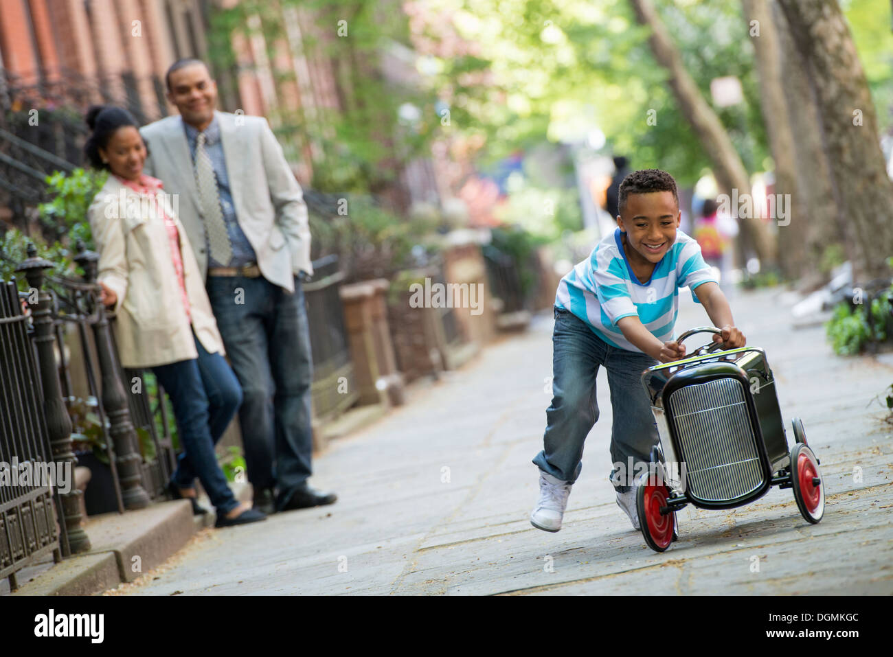 Ein kleiner Junge spielt mit einem alten altmodischen Spielzeugauto auf Rädern auf einer Stadtstraße. Ein paar auf der Suche auf. Stockfoto