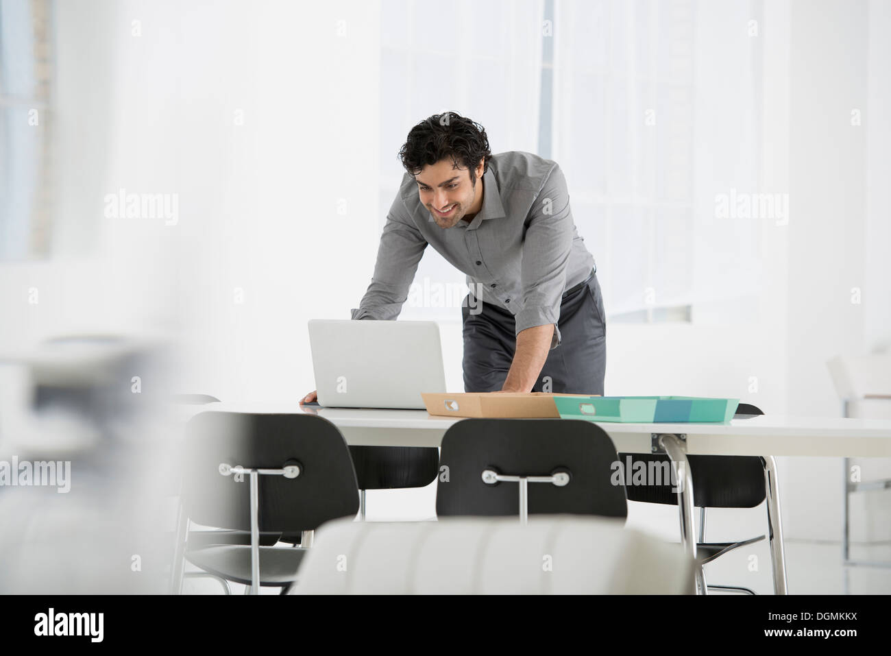 Geschäft. Ein Mann steht über einen Schreibtisch, lehnt sich nach unten, einen Laptop-Computer zu verwenden. Stockfoto