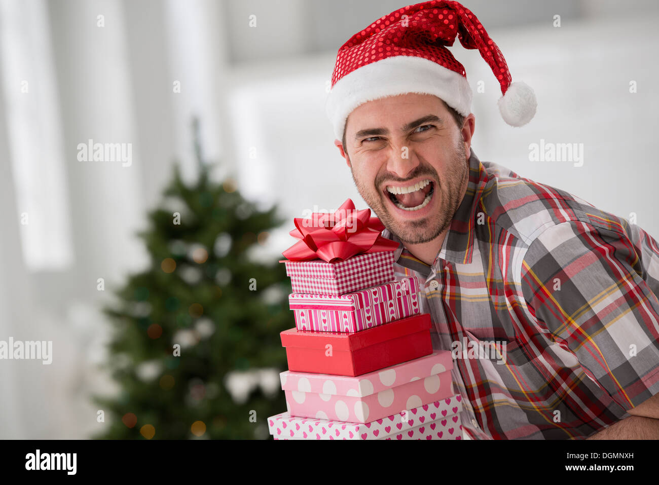 Büroeinrichtung. Weihnachten zu feiern. Ein Mann in eine Weihnachtsmütze hält einen Stapel von Geschenken. Geschmückter Weihnachtsbaum. Stockfoto