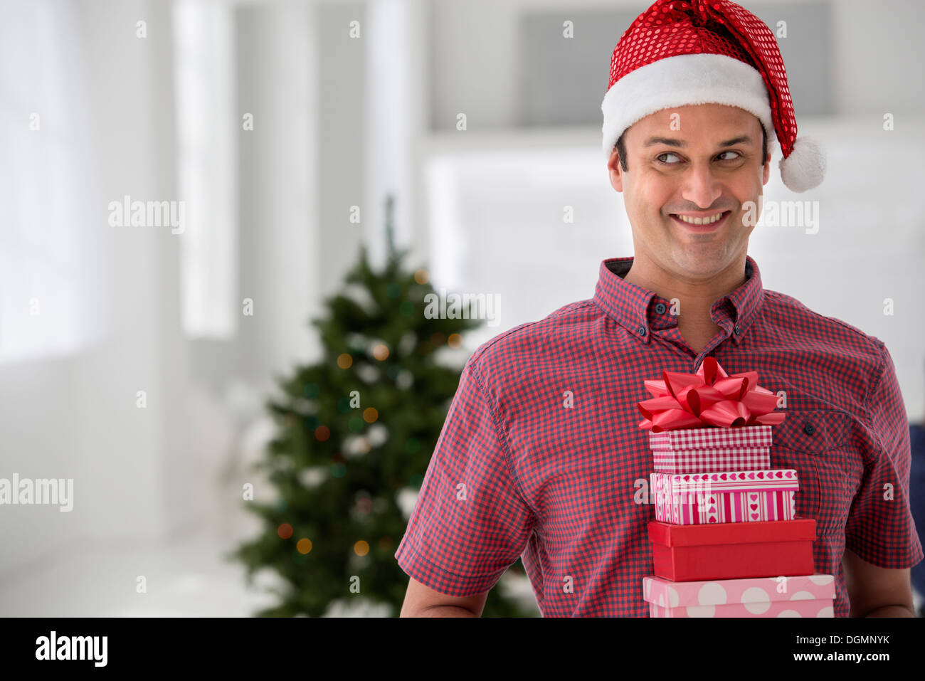 Büroeinrichtung. Weihnachten zu feiern. Ein Mann in eine Weihnachtsmütze hält einen Stapel von Geschenken. Geschmückter Weihnachtsbaum. Stockfoto