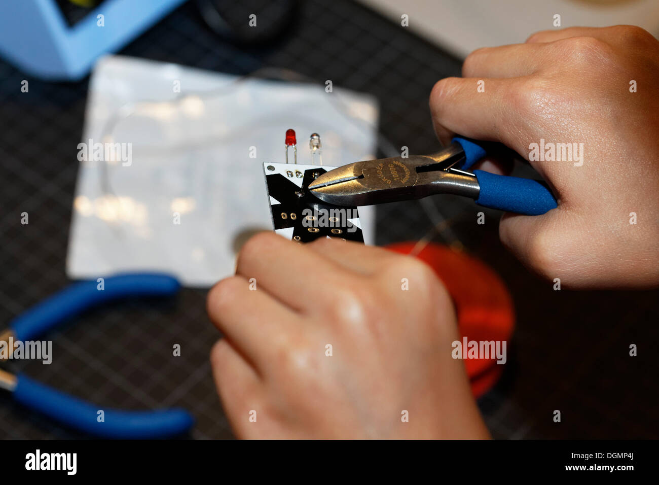 Hände mit einer Zange auf ein elektronisches Bauteil mit lichtemittierenden Dioden, IdeenParks 2012, Technologie und Bildung des Kindes Stockfoto