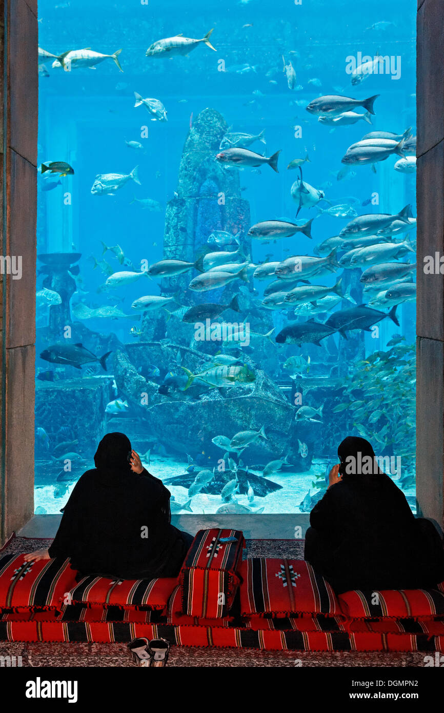 Zwei arabische Frauen reden über ihre Handys vor ein Aquarium in den Lost Chambers, ein Themenpark, basiert auf der Legende von Stockfoto