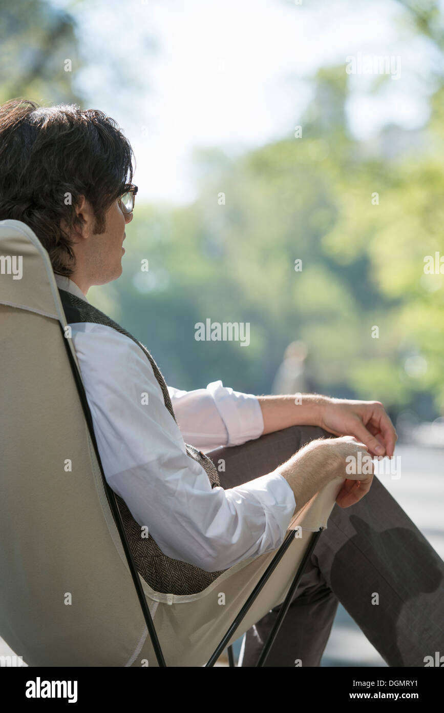 Leben in der Stadt. Ein Mann sitzt in einer Leinwand Campingstuhl im Park. Stockfoto