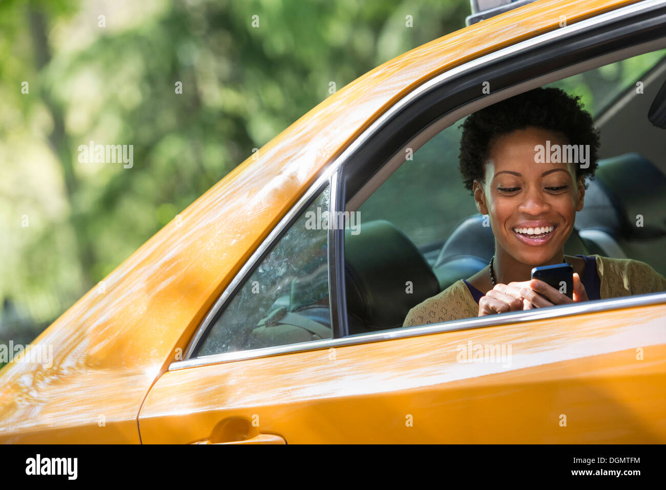 Eine Frau sitzt auf dem hinteren Beifahrersitz ein yellow Cab überprüft ihr Telefon. Stockfoto