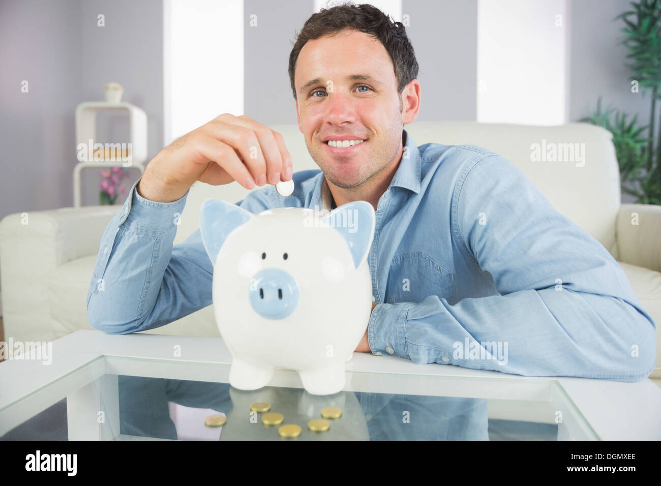 Gut aussehende legerer Mann, Münze in Sparschwein Stockfoto