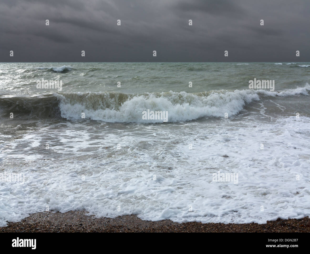 Rauer See brechen auf einem Kiesstrand mit einem stürmischen Himmel am Horizont, Worthing, England Stockfoto