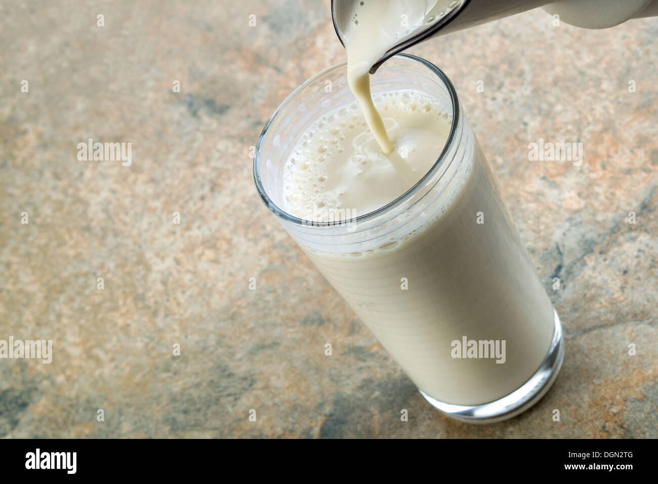 Horizontale Foto von Krug gießen Mandelmilch in Glas mit Stein Zähler nach oben im Hintergrund Stockfoto