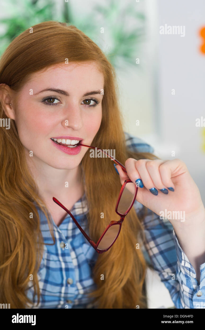 Lächelnde Rothaarige beißen ihre Lesebrille Stockfoto