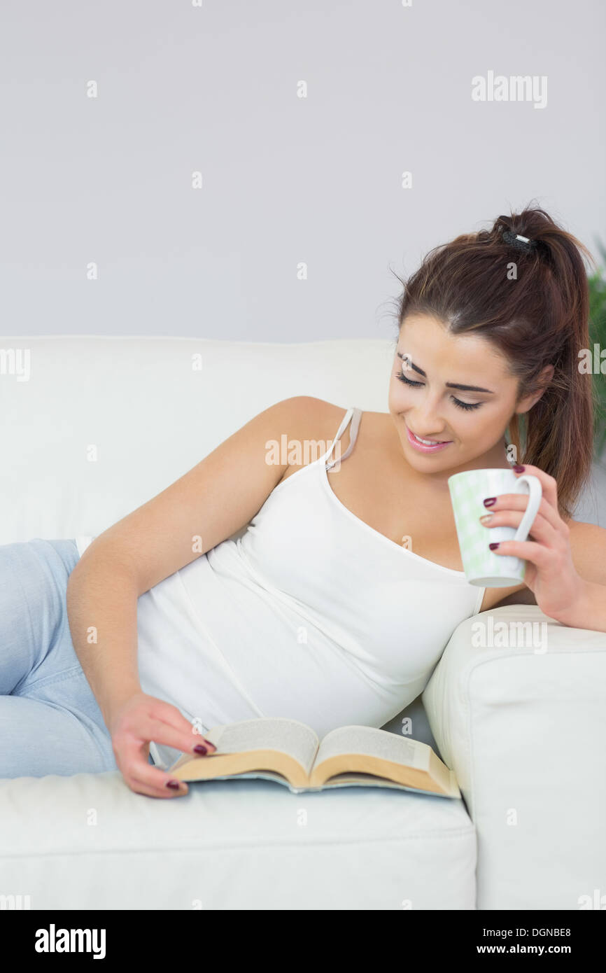 Hübsche Frau, ein Buch lesen und Kaffeetrinken amüsiert Stockfoto