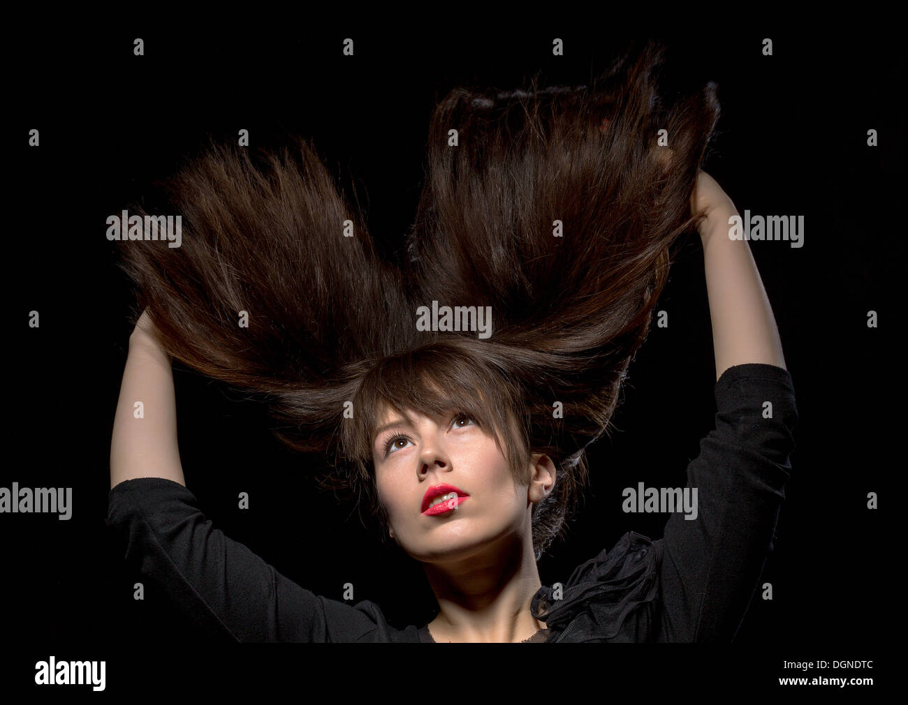 Junge Frau mit ihrem lange gerade brünette Haare fliegen in der Luft und ihre Arme über den Kopf, isoliert auf schwarz Stockfoto