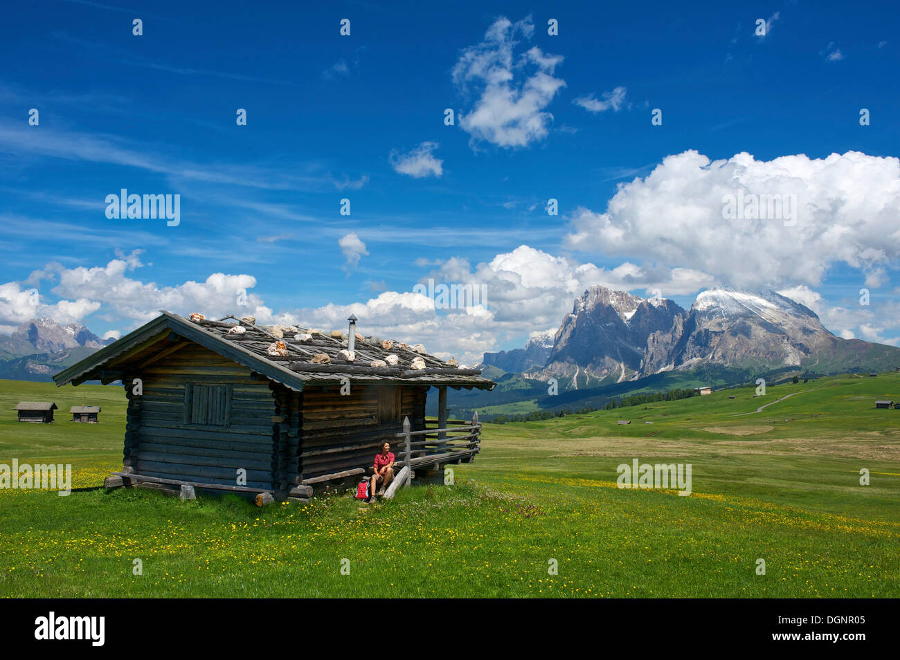Frau sitzt auf einer Almhütte vor Piatto Berg- und Sasso Lungo Berge, Seiser Alm, Dolomiten Stockfoto
