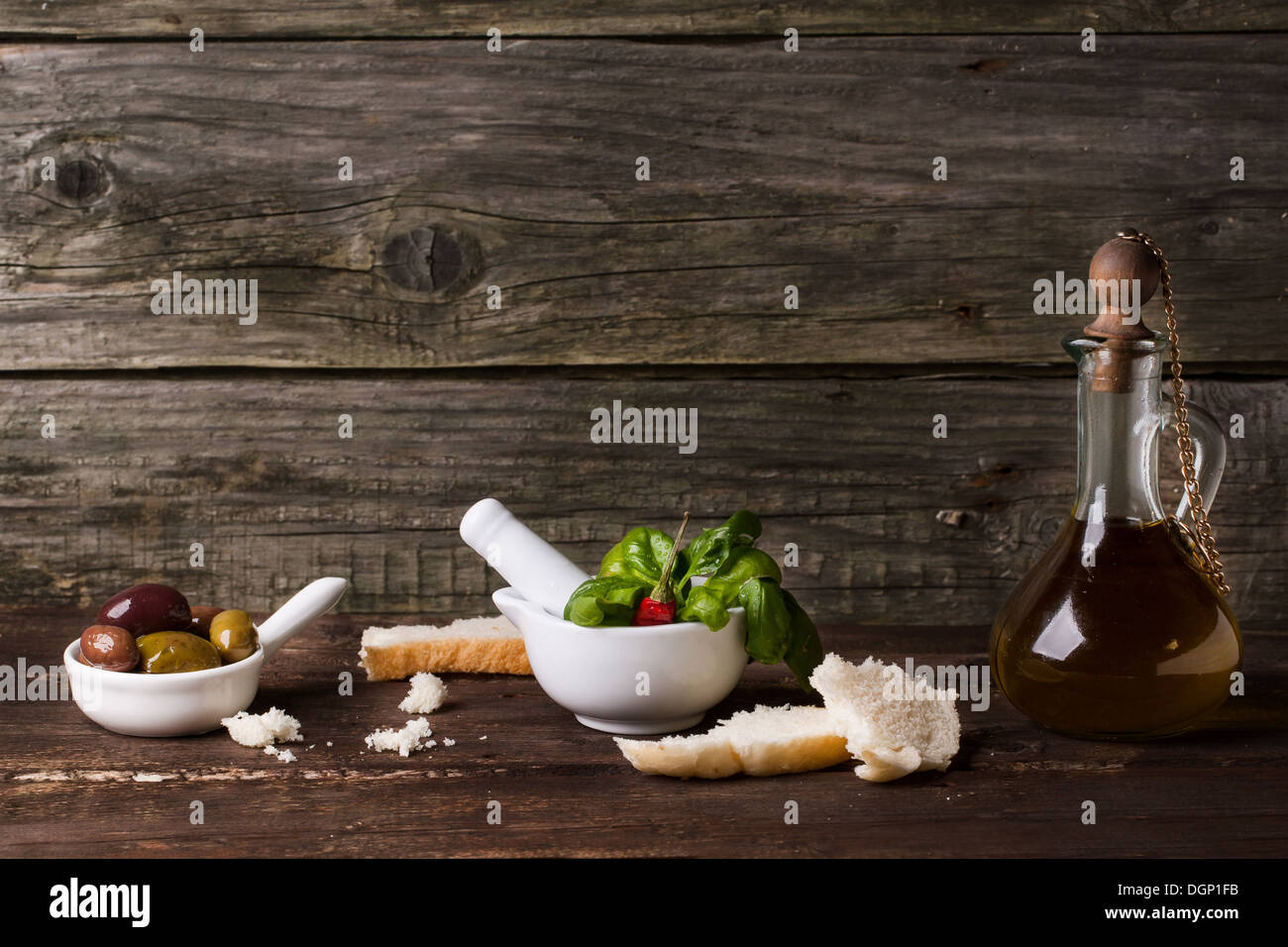 Vintage Flasche Olivenöl mit Schalen von Oliven, frischem Basilikum und Scheiben Brot auf alten Holztisch Stockfoto
