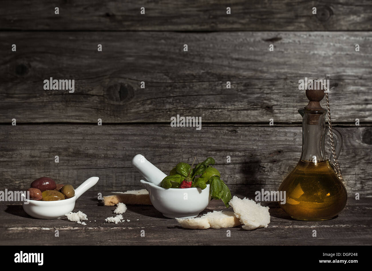 Vintage Flasche Olivenöl mit Schalen von Oliven, frischem Basilikum und Scheiben Brot auf alten Holztisch Stockfoto