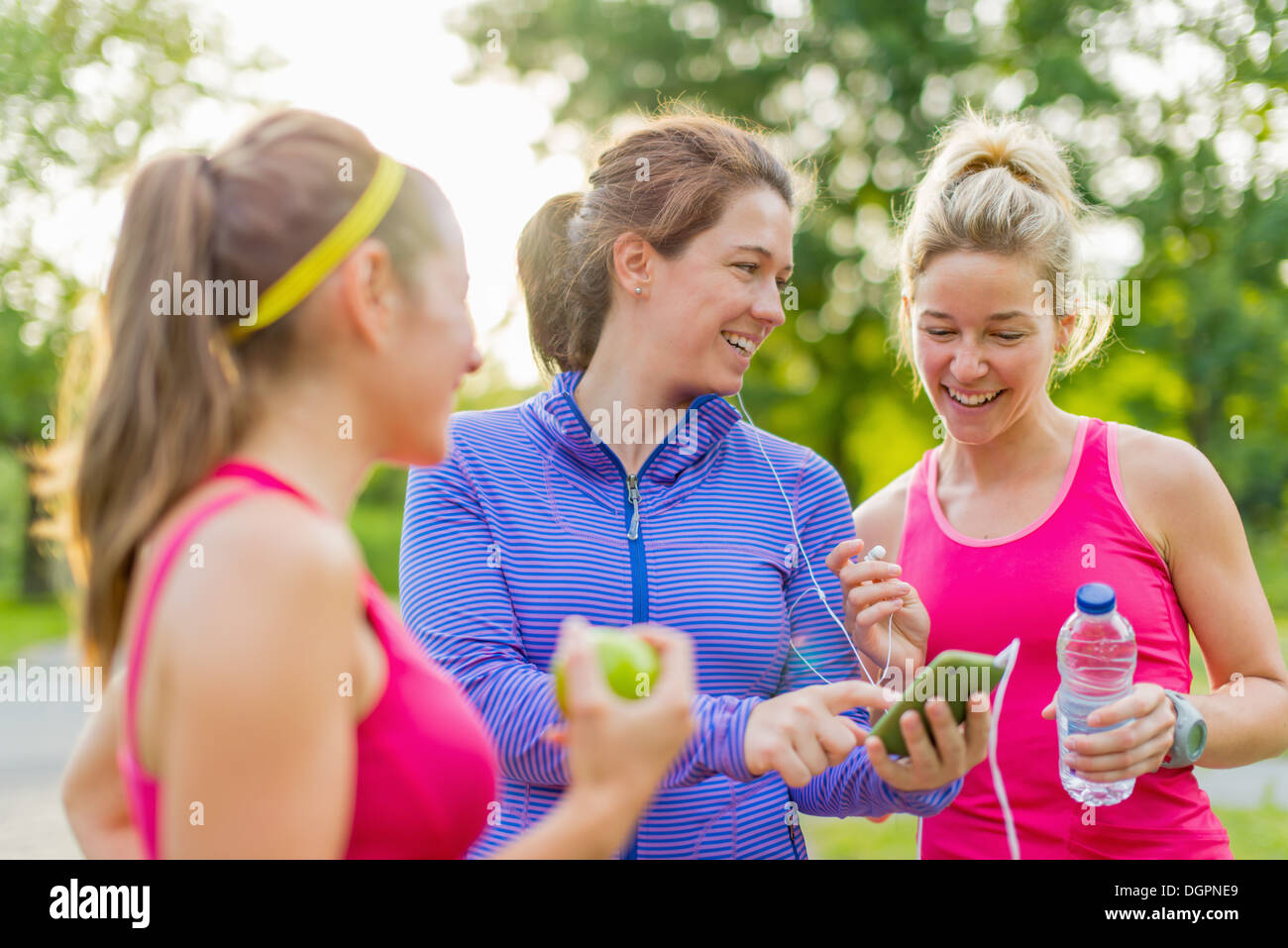 Gruppe von glücklich aktive Mädchen, die Vorbereitung für einen Lauf in Natur durch die Wahl der Musik auf einem Smartphone Stockfoto