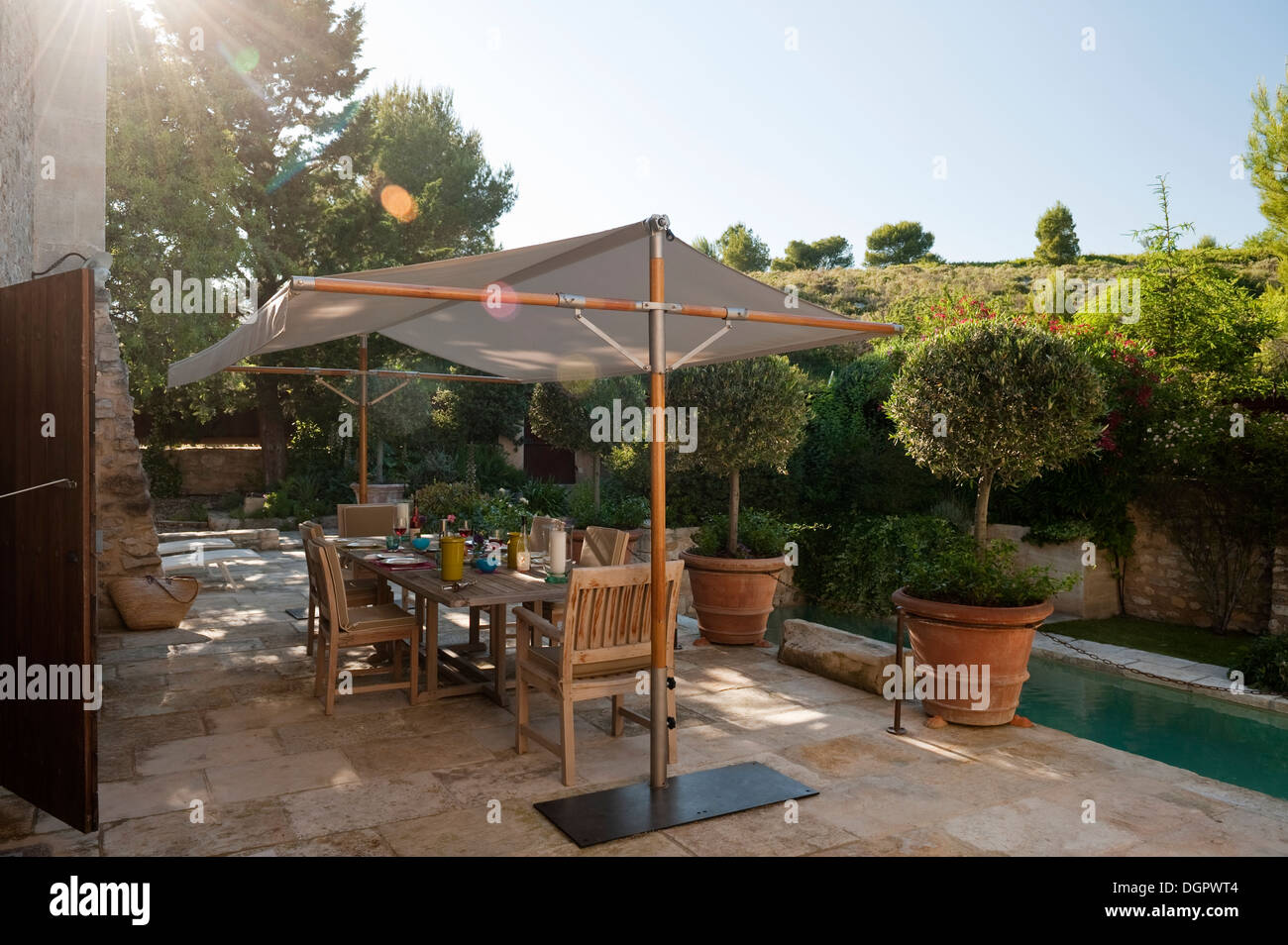 Eine Terrasse am Pool mit großem Tisch, Stühlen und Sonnenliegen Schirm alle von Tectona eingerichtet. Stockfoto