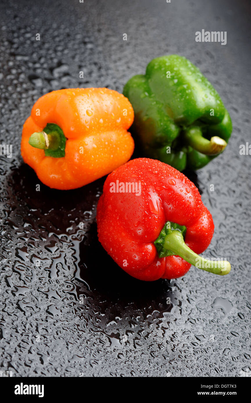 Orange, rote und grüne Paprika auf schwarzen Tisch nach Regen Stockfoto