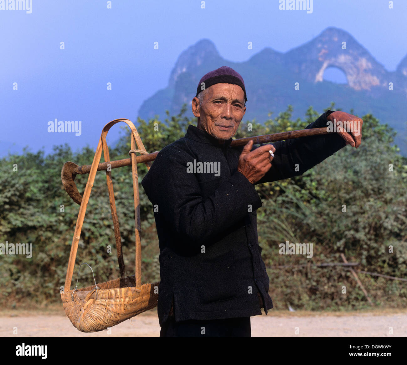 Mann trägt eine Last mit einer Schulter-Pole vor Mond Berg in der Nähe von Yangshuo, Guilin, Guangxi, China, Asien Stockfoto