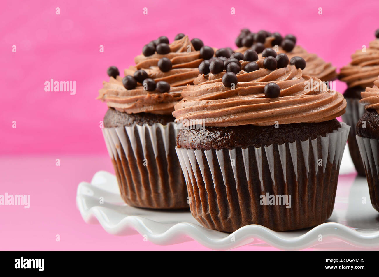 Gourmet-Schokolade Cupcakes mit Schokoladenglasur chiffon und Schokokugeln auf weißen Kuchen stehen mit einem tief rosa Hintergrund Stockfoto