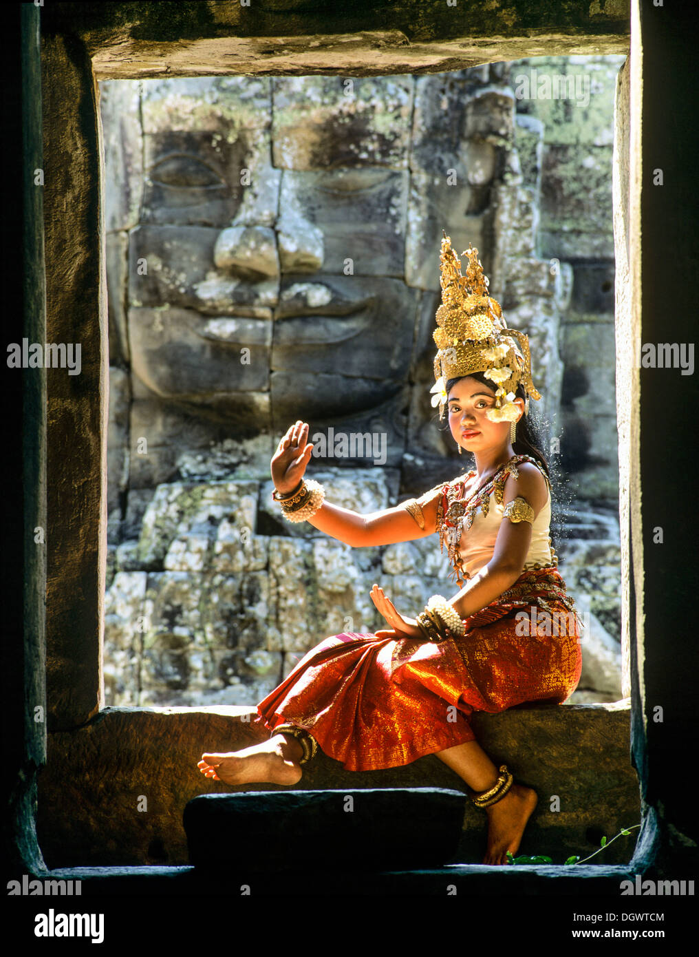 Tempel-Tänzerin oder Apsara sitzen in einem Fenster vor einem Gesicht Turm am Bayon-Tempel, UNESCO Weltkulturerbe Stockfoto