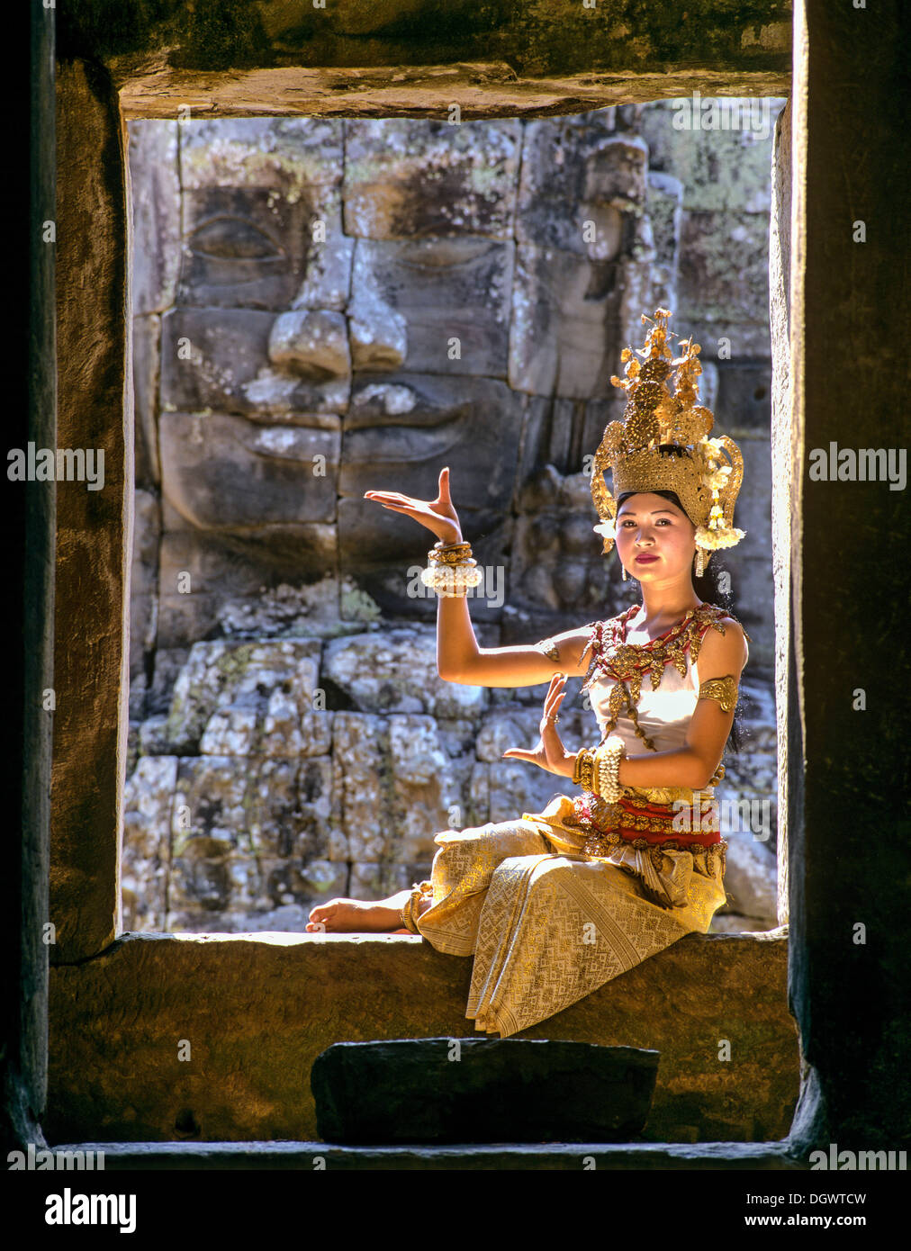 Tempel-Tänzerin oder Apsara sitzen in einem Fenster vor einem Gesicht Turm am Bayon-Tempel, UNESCO Weltkulturerbe Stockfoto