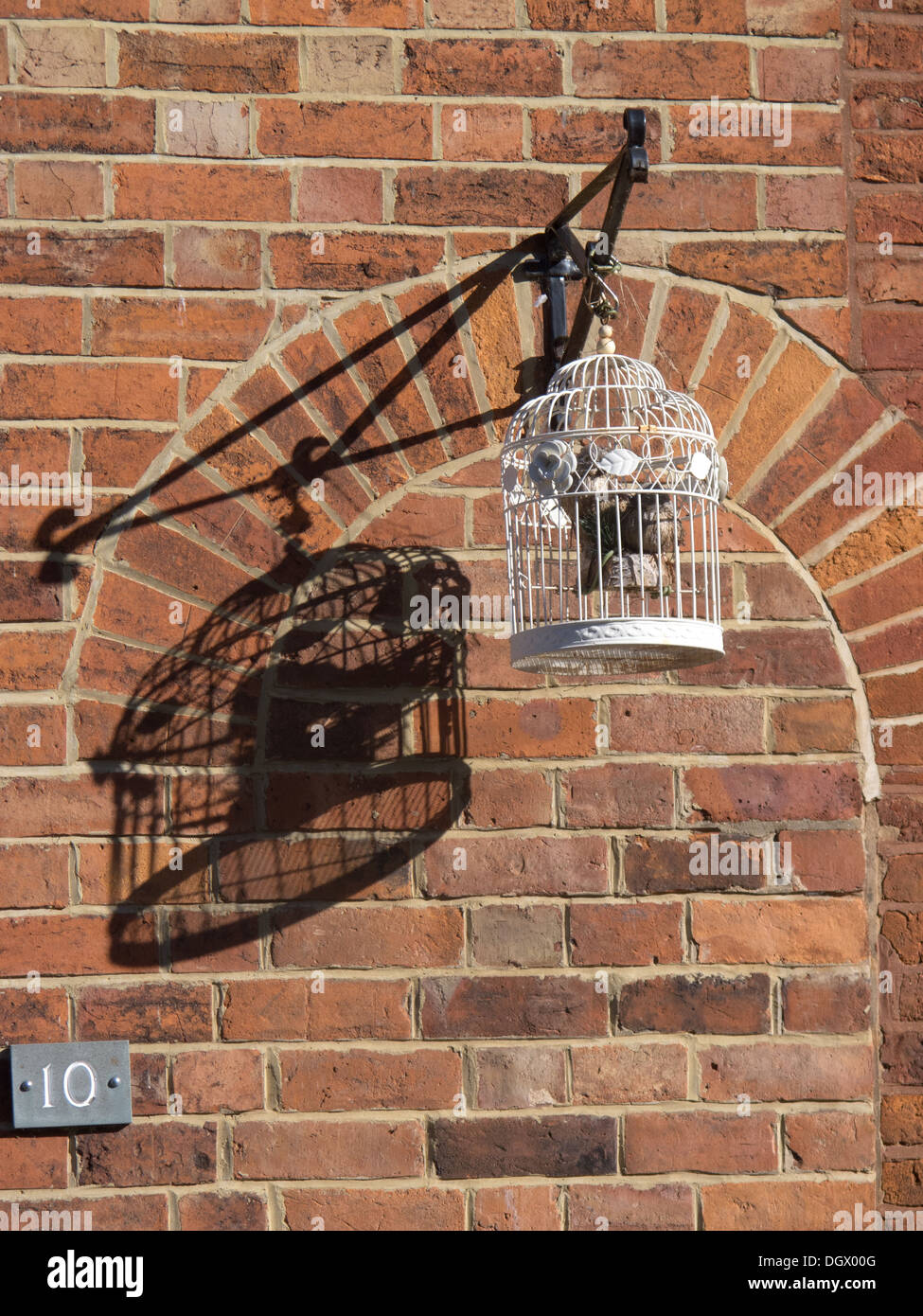 Leeren Vogelkäfig werfen Schatten auf roten Backsteinmauer Stockfoto