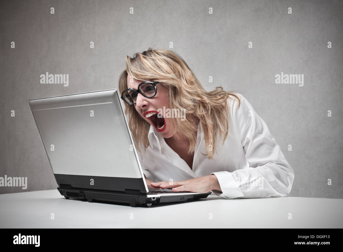 Böse blonde Frau schreiend gegen einen laptop Stockfoto
