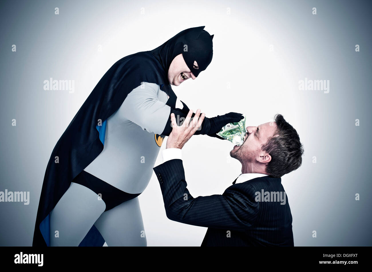 Mollig Superhelden in einem Batman-Kostüm Füllung Geld in den Mund von einem Mann in einem Anzug Stockfoto
