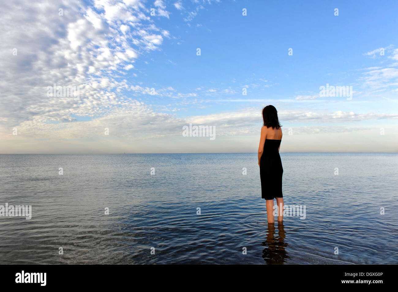 Frau trägt ein schwarzes Kleid stehend im Wasser des Meeres, launisch Wolken, Cavallino, Jesolo, Venedig, Italien Stockfoto