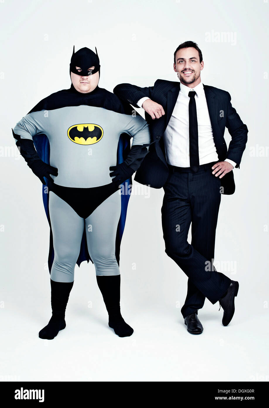 Sportlicher Mann in einem Anzug neben einem dicken Mann gekleidet wie ein Superheld Batman Stockfoto