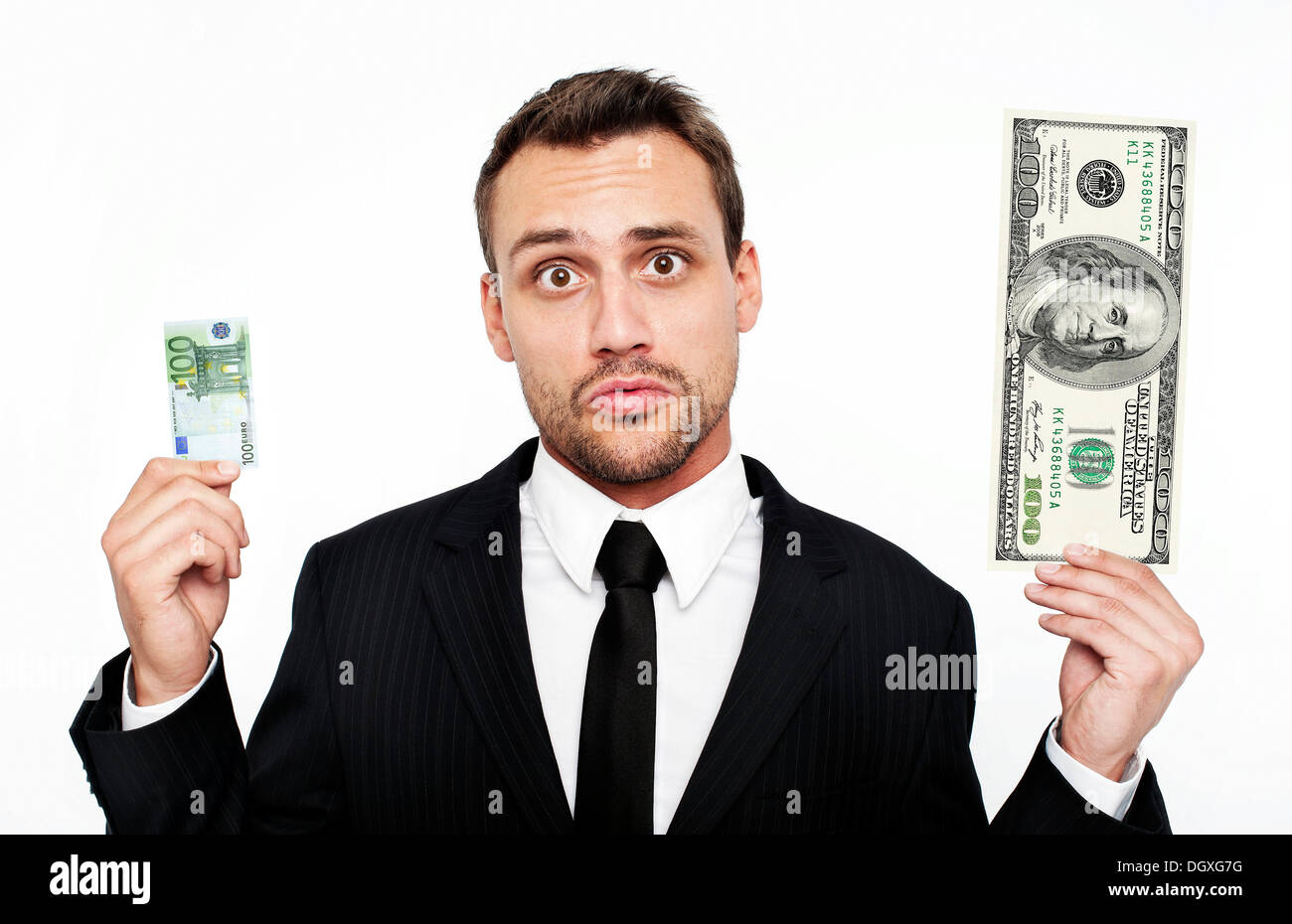 Frustrierte junge Mann trägt einen Anzug hält eine kleine 100 Euro-Banknote und einen großen 100 Dollarschein, Österreich Stockfoto