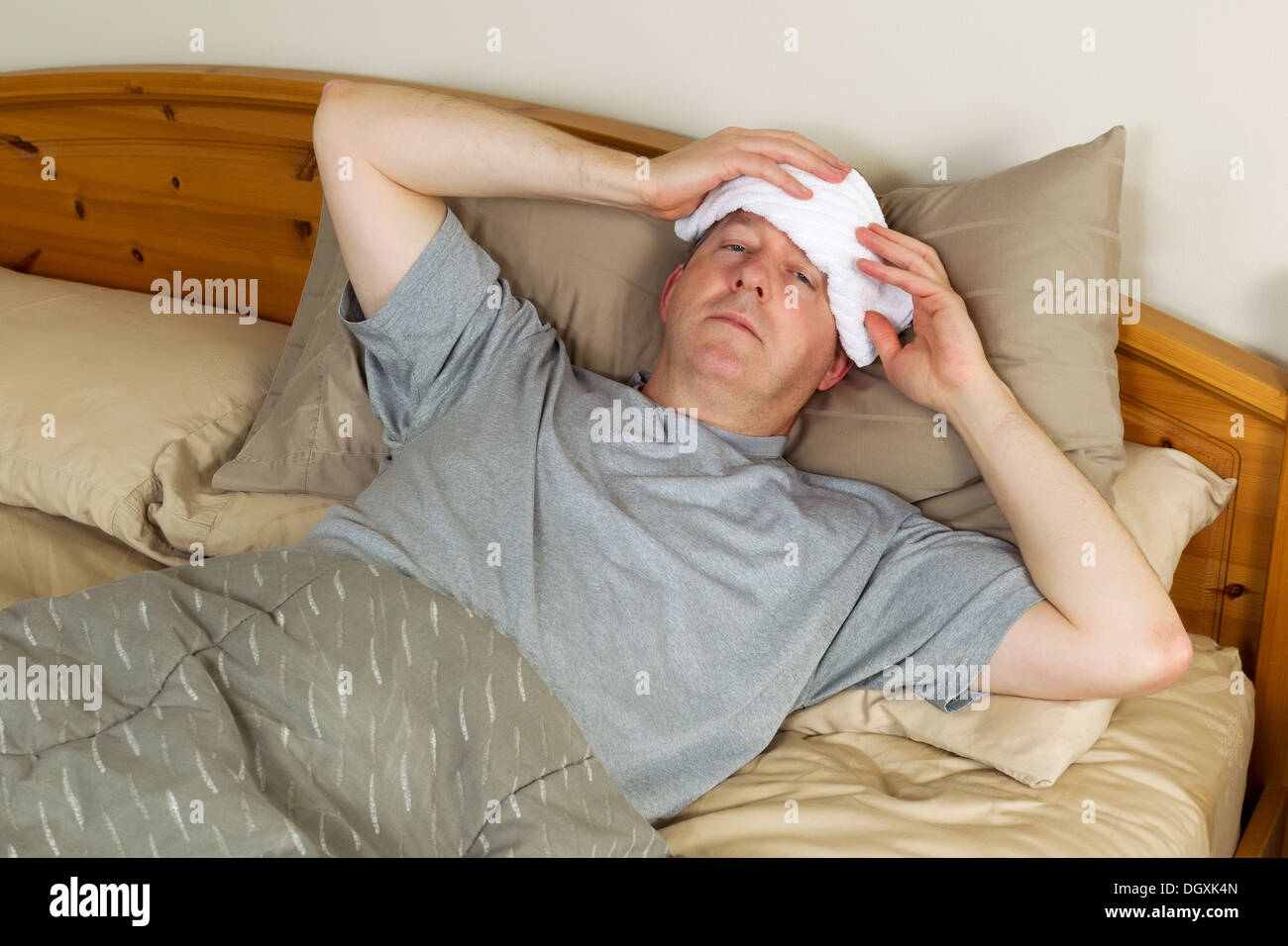 Horizontale Foto des reifen Mannes, die Behandlung von Fieber durch  Waschlappen an die Stirn halten, beim liegen im Bett Stockfotografie - Alamy