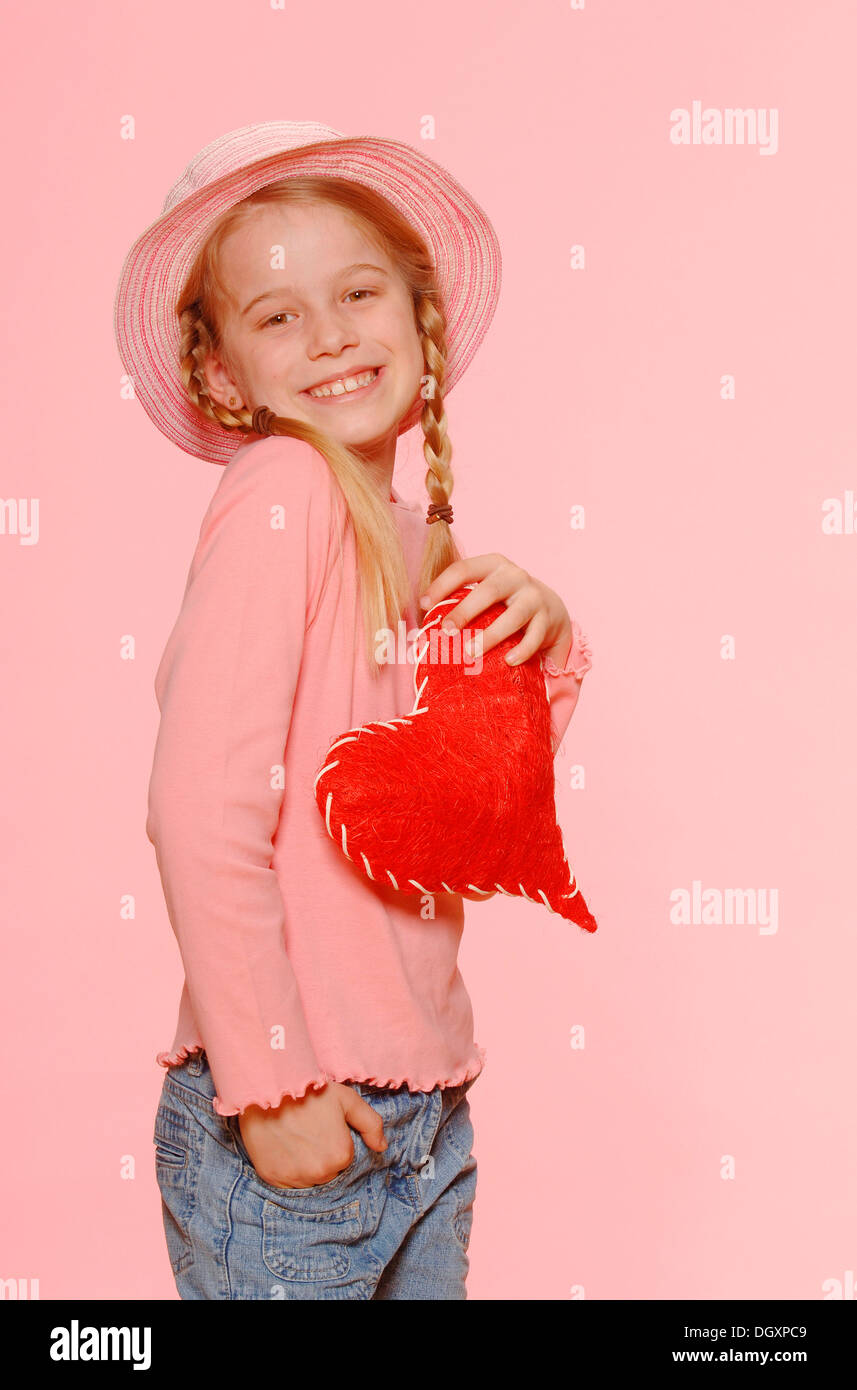 Mädchen mit Zöpfen, trägt einen Hut und hält ein rotes Herz Stockfoto