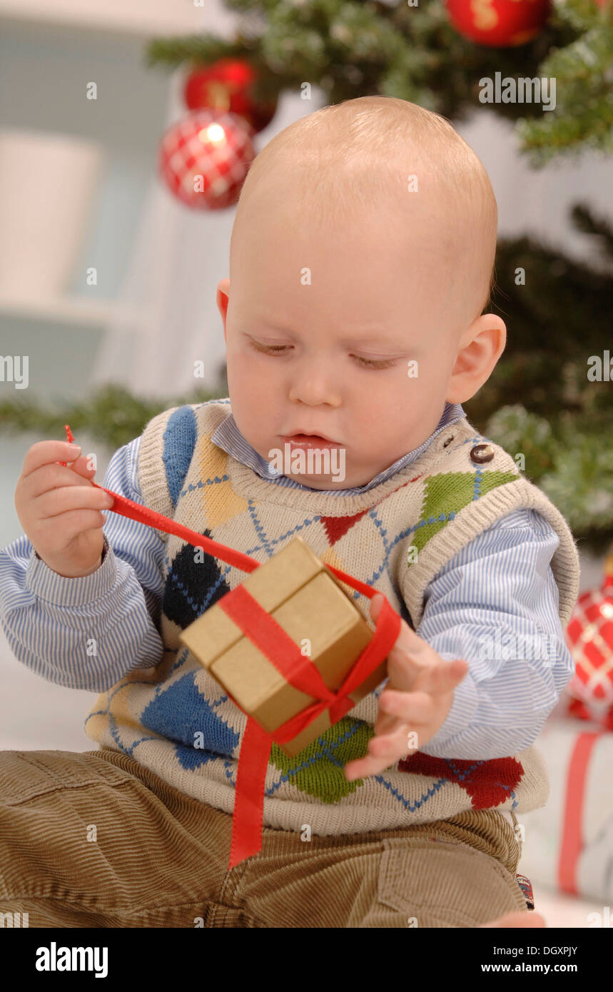 Kleinkind ein goldenes Geschenk vor eines Weihnachtsbaums Auspacken Stockfoto