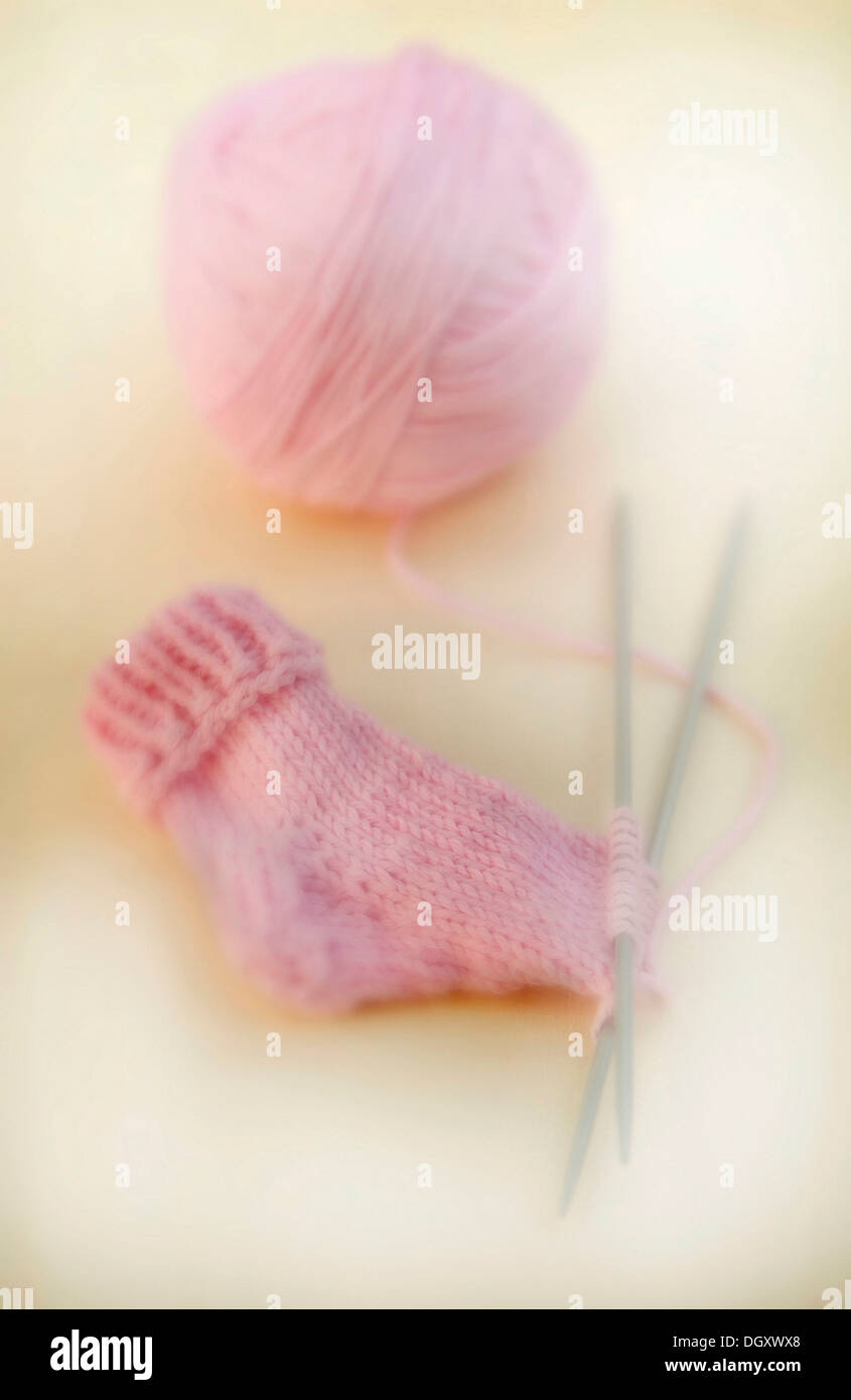 Halbfertige gestrickte rosa Baby-Socke mit einem Ball aus Wolle und Stricknadeln Stockfoto