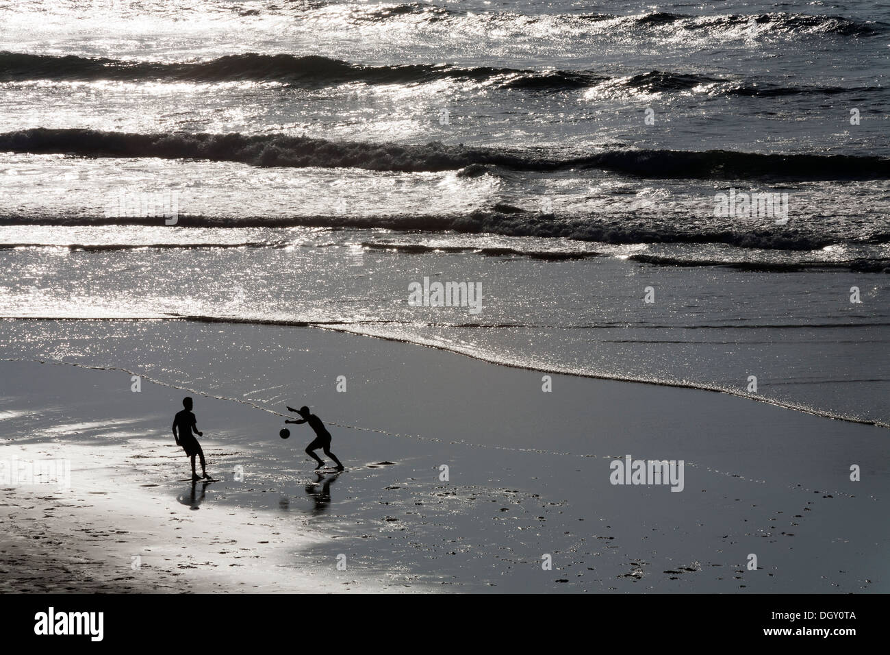 Silhouettenhafte Figuren von zwei jungen Männern, die Fußball spielen auf einem Strand vor dem Hintergrund des Meeres und hellem Sonnenlicht Stockfoto