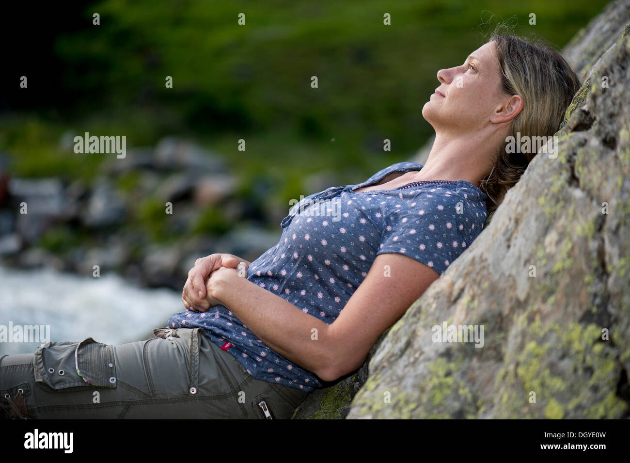 Frau, Anfang 40, verträumt an einem Felsen gelehnt Stockfoto