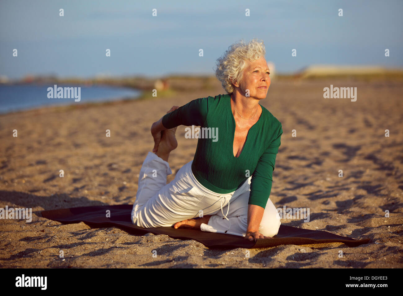 Ältere Frau in stretching Lage am Meer am Morgen. Ältere Frau beim Yoga am Strand. Stockfoto