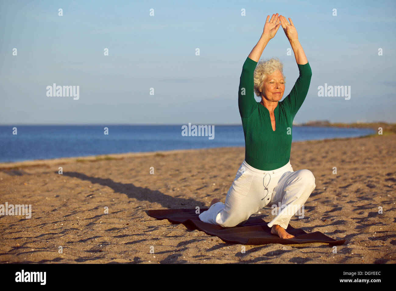 Ältere Frau praktizieren Yoga-Posen am Sandstrand. Ältere kaukasischen Frau Dehnung der Beine und Arme am Ufer des Meeres. Stockfoto