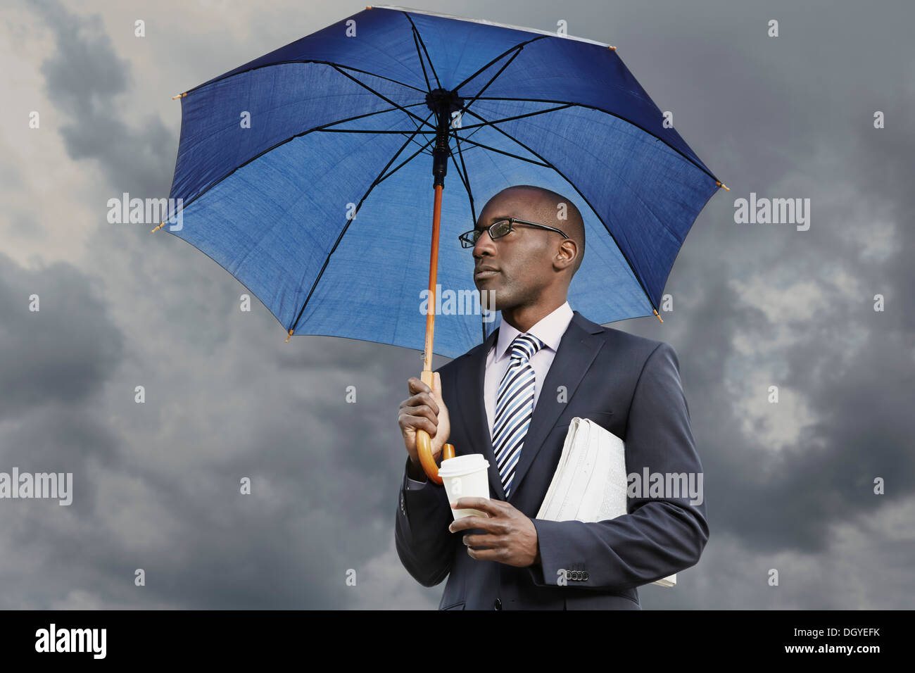 Geschäftsmann mit Sonnenschirm, Einweg Kaffee und Zeitung unter ein stimmungsvoller Himmel Stockfoto