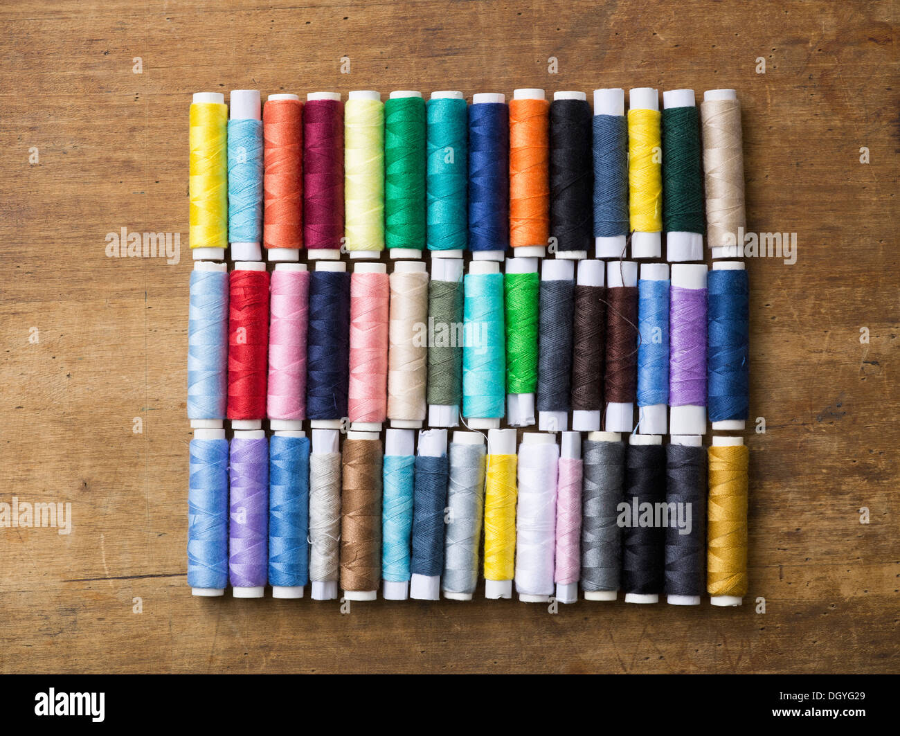 Reihen von verschiedenen farbigen Spulen des Threads auf einem Holztisch Stockfoto