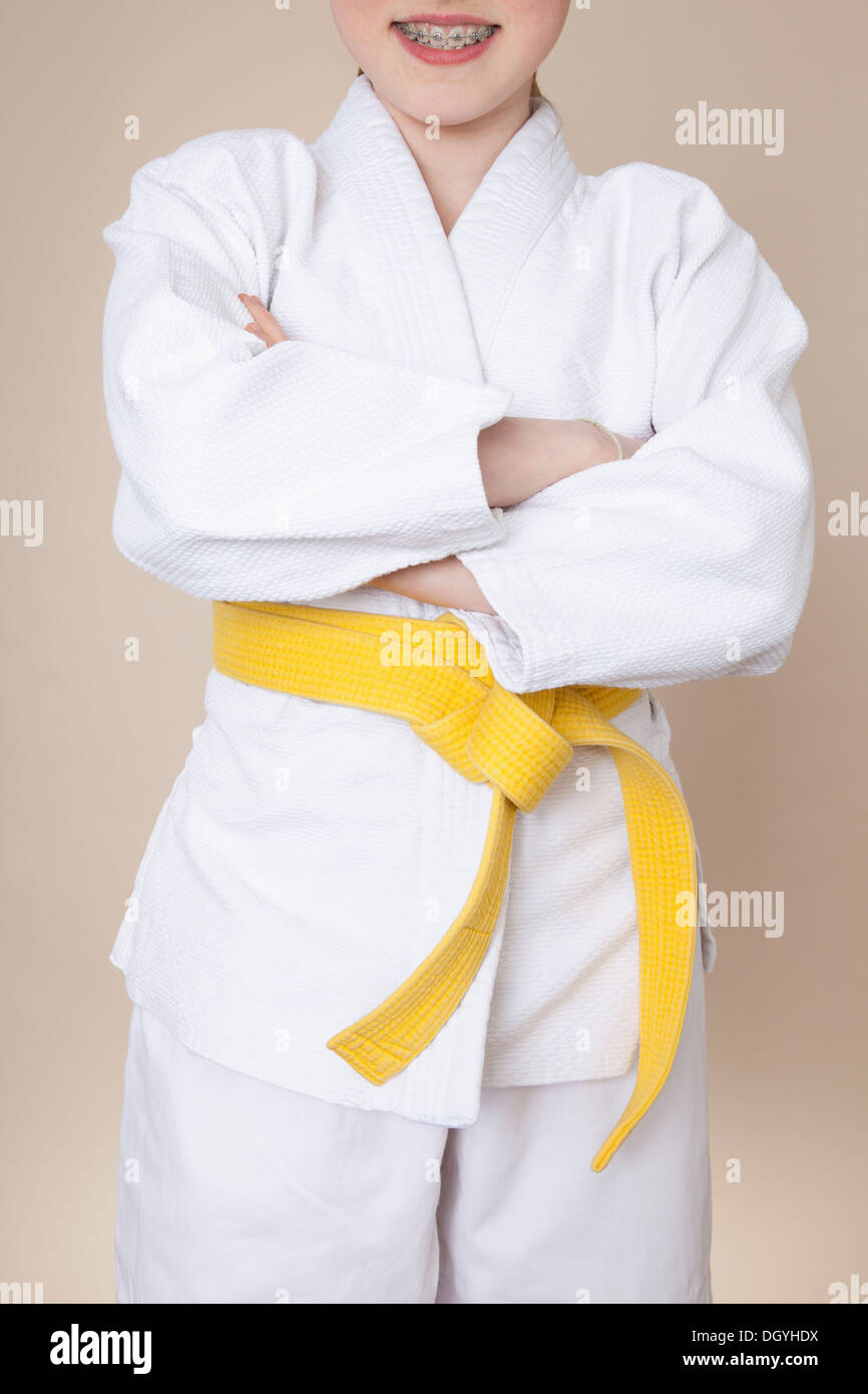 Eine lächelnde Mädchen mit Armen gekreuzt tragen Kampfkunst uniform mit gelber Gürtel Stockfoto