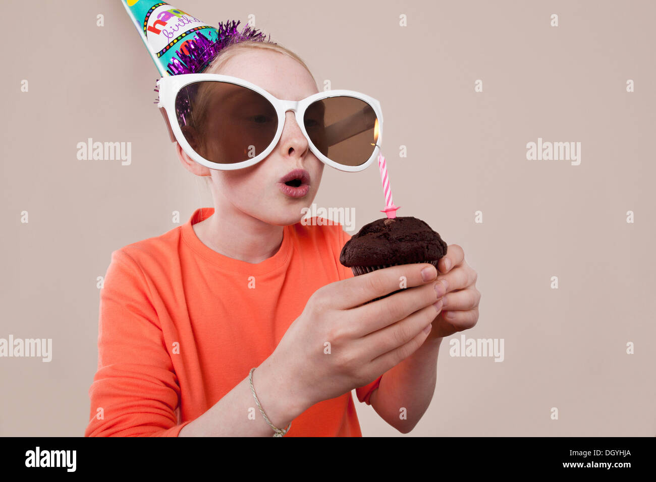 Ein Mädchen trägt Neuheit Sonnenbrillen und Partyhut Geburtstag Kerze ausblasen Stockfoto
