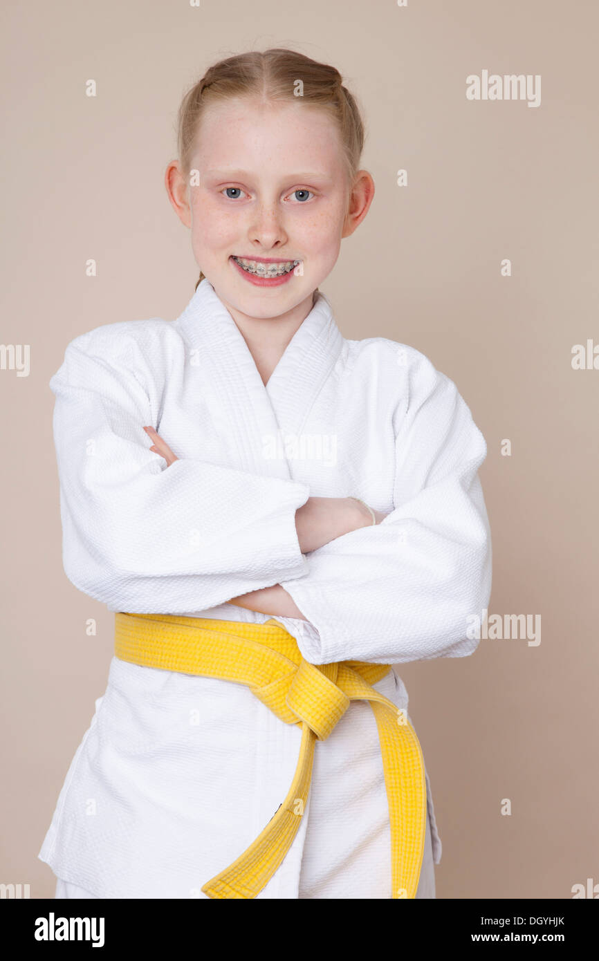 Eine lächelnde Mädchen mit Armen gekreuzt tragen Kampfkunst uniform mit gelber Gürtel Stockfoto