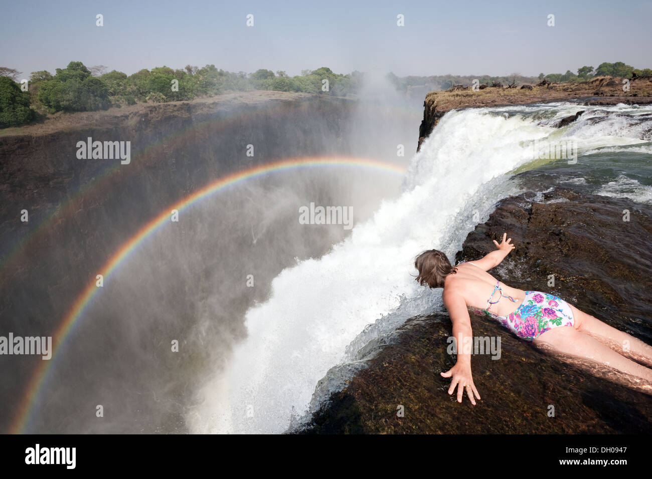 Applying kaukasischen Frau, die über den Rand der Victoriafälle in Devils Pool, Beispiel für Abenteuerurlaub, Sambia Afrika Stockfoto