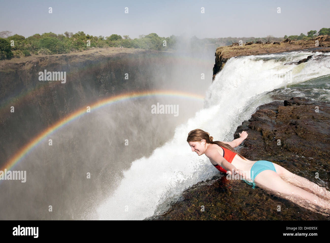 Eine junge Frau, die am Rande des Devils Pools, Victoria Falls, auf der Livingstone Island, Sambia Africa, hängt - Abenteuerurlaub Stockfoto