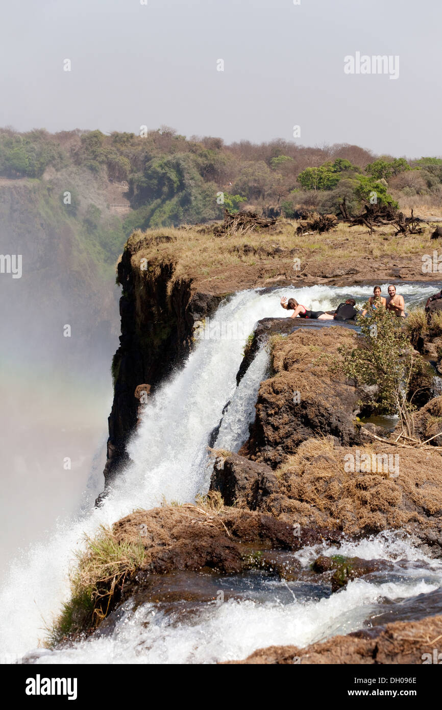 Touristen in Devils Pool mit Blick über den Rand der Victoriafälle, Insel Livingstone, Sambia Afrika Stockfoto